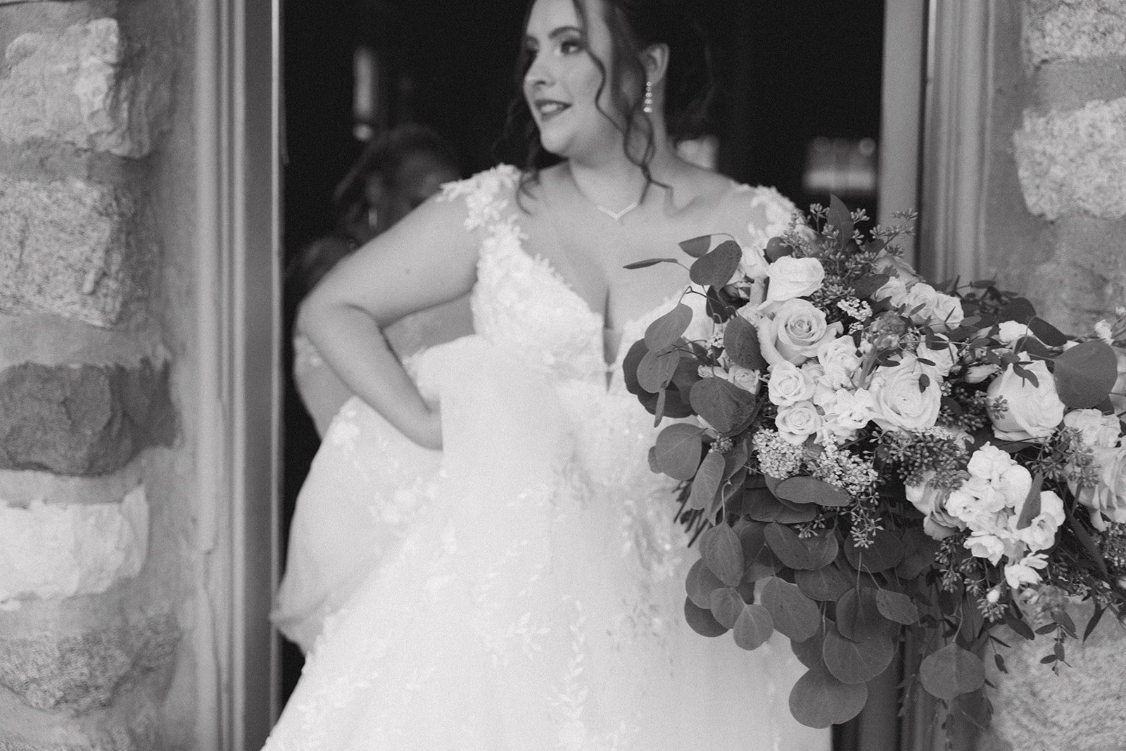 Black and white portrait of the bride holding a cascading bouquet beneath a stone arch