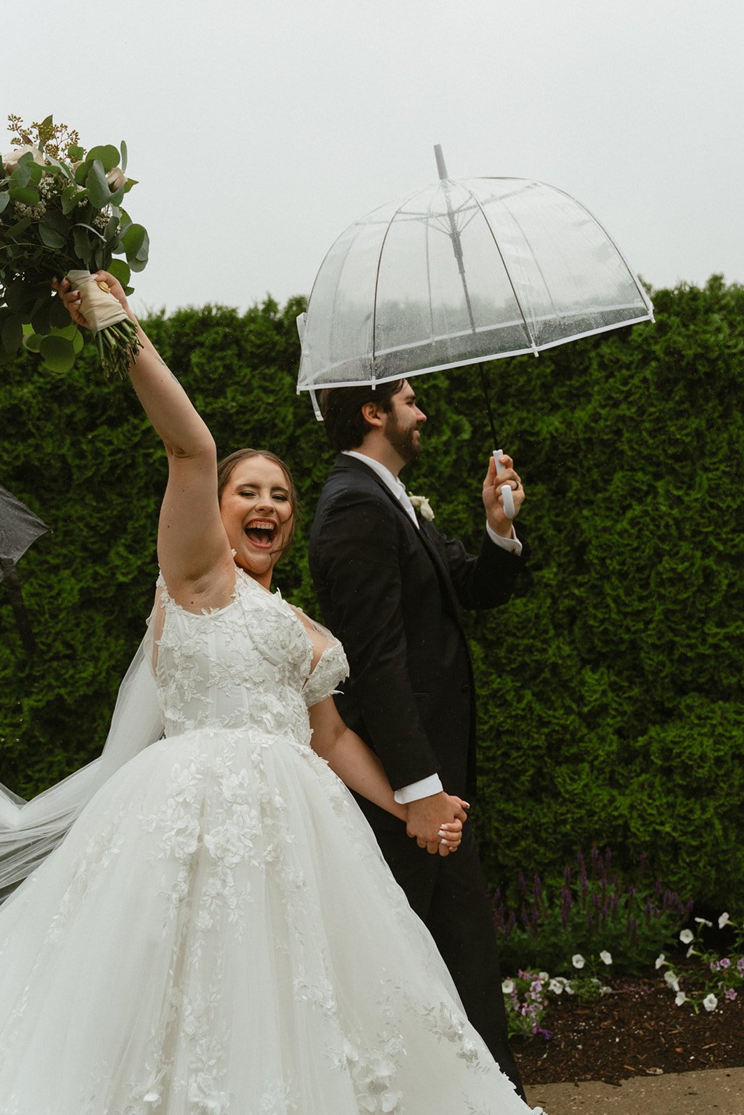 Bride and groom sharing a moment under a clear umbrella beside florals