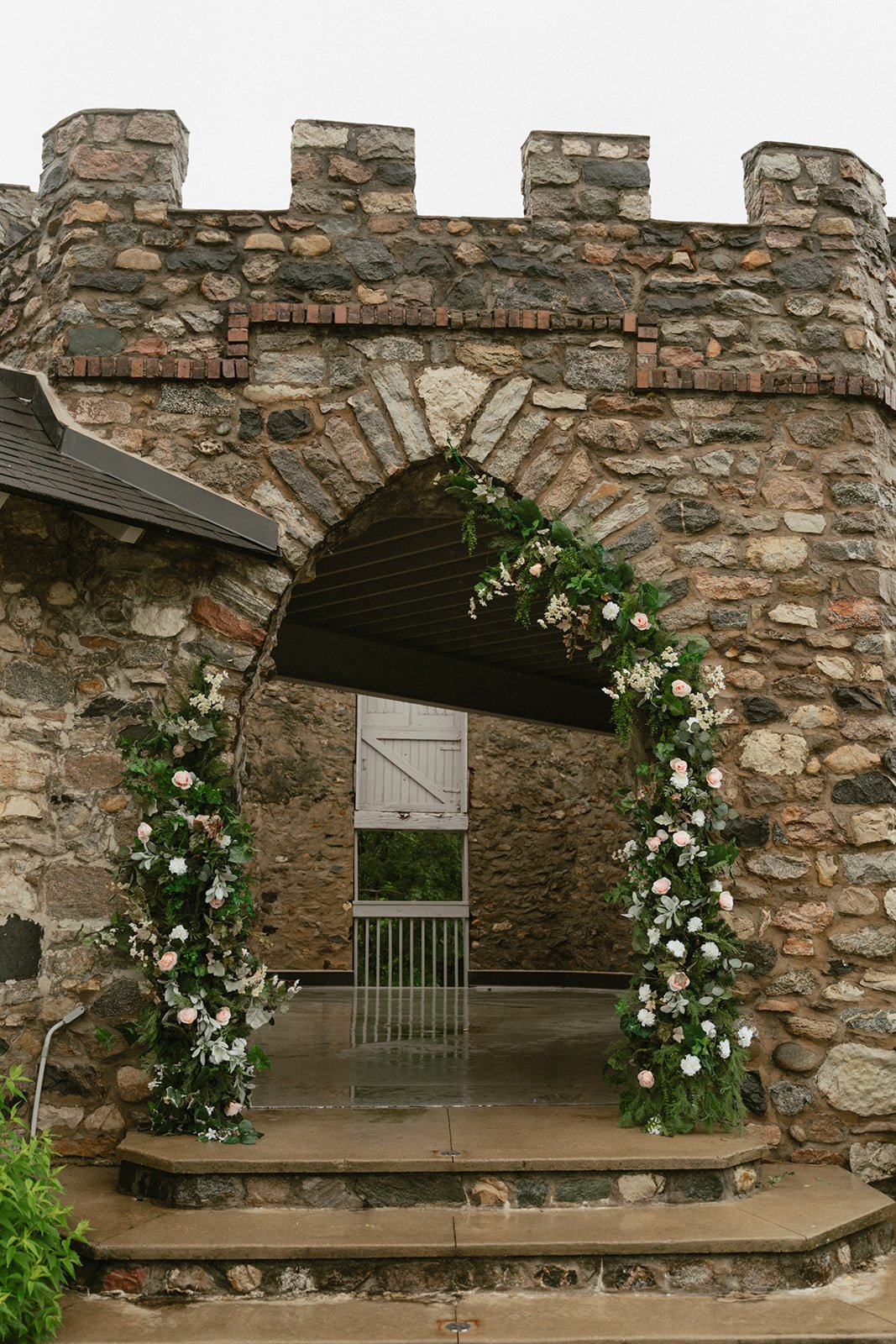 Greenery arch framing stone castle ruins at the ceremony site